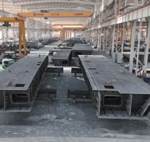 Large fabricated steel box-girder components are arranged inside an East Baoyu workshop.