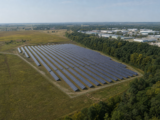 Conceptual oblique view of a solar array adjoining open farmland, a tree belt and low industrial development.